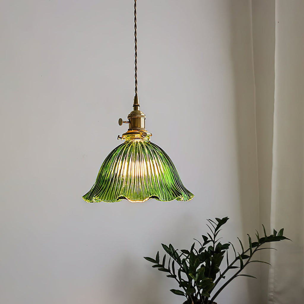 This Clérachic pendant glowing in a bright corner, its green ribbed shade hung beside a sheer curtain and a leafy plant.