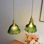 Pair of Clérachic green ribbed pendants lit above a wooden table, with pink flowers and a framed picture to one side.