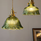 Warm light through the fluted green glass of this Clérachic pendant, with a second shade and a framed picture behind.