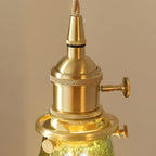 Close view of the knurled brass lamp holder and thumb screws where the cord meets the green glass on this Clérachic pendant.