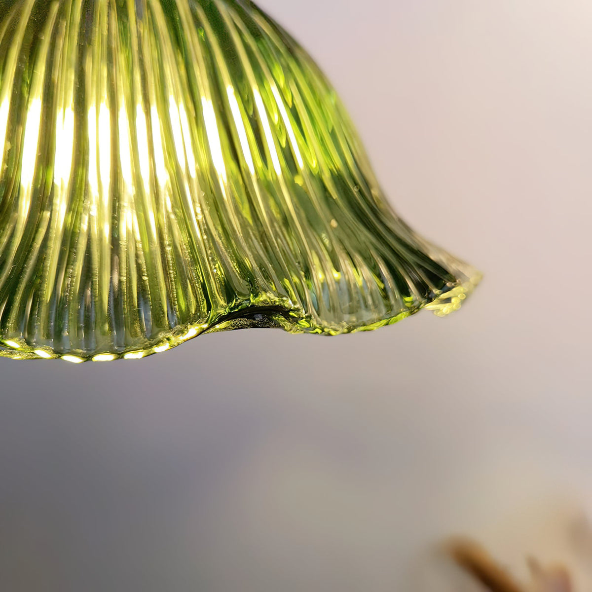 Close view of the ruffled lower edge of the ribbed green glass shade, lit from inside, on this Clérachic pendant.