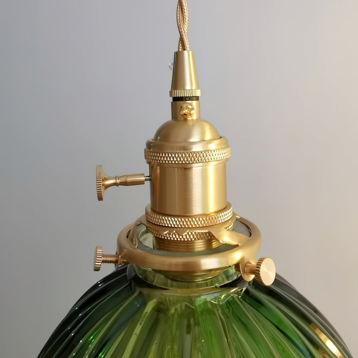 Close view of the brass socket, collar and fixing screws holding the dark-green ribbed shade on this Clérachic pendant.