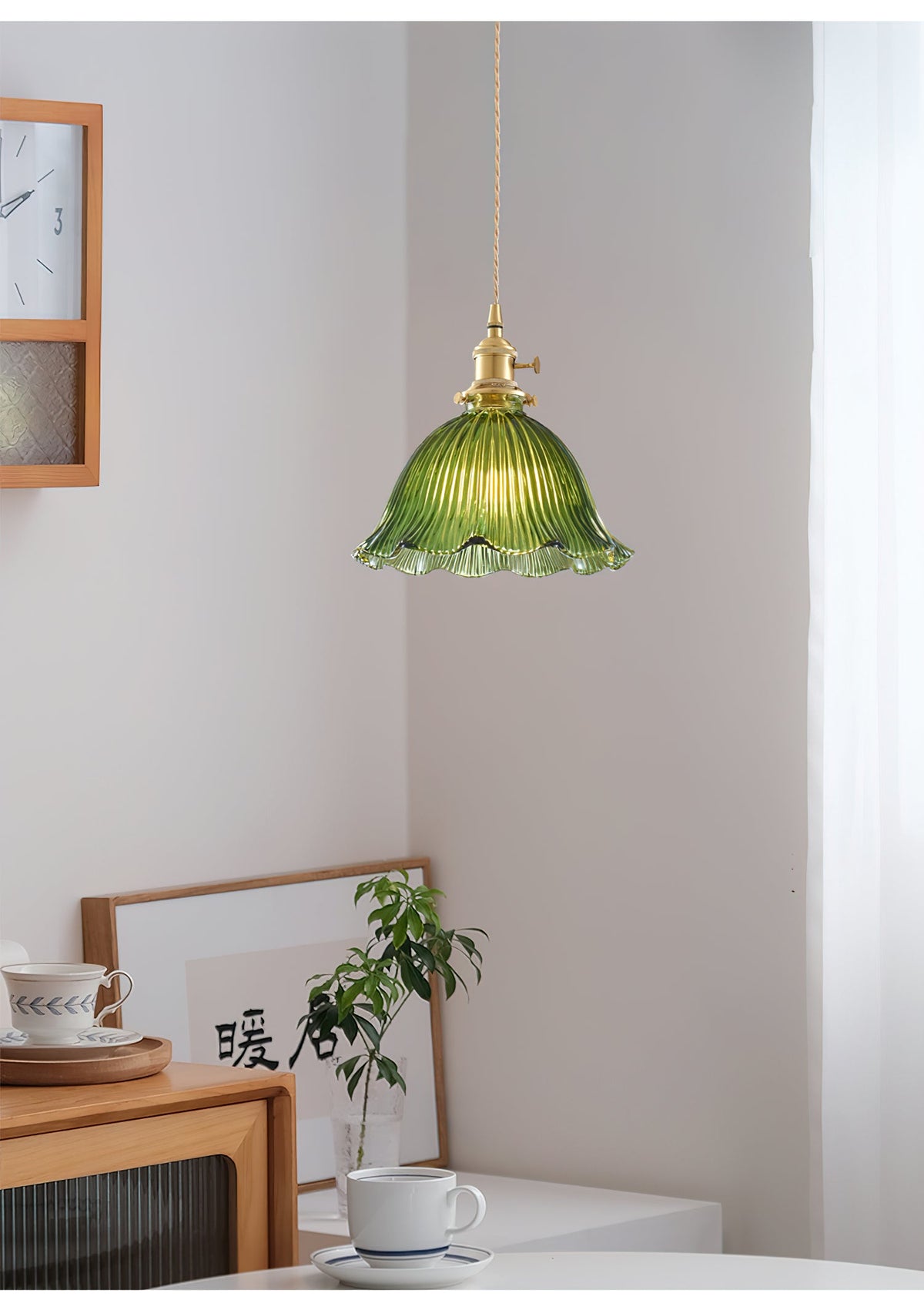 Small green glass pendant hanging in a quiet corner above a wooden cabinet and a cup, a lamp from Clérachic.