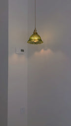 Distant view of a lit green glass pendant in a grey corner, casting soft light on the wall, from Clérachic.