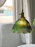 Lit green glass pendant by a bright window with white curtains, its ribbed shade glowing warm, from Clérachic.