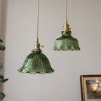 Two green fluted glass pendants with brass cord fittings hanging near a leafy plant and a framed picture, from Clérachic.