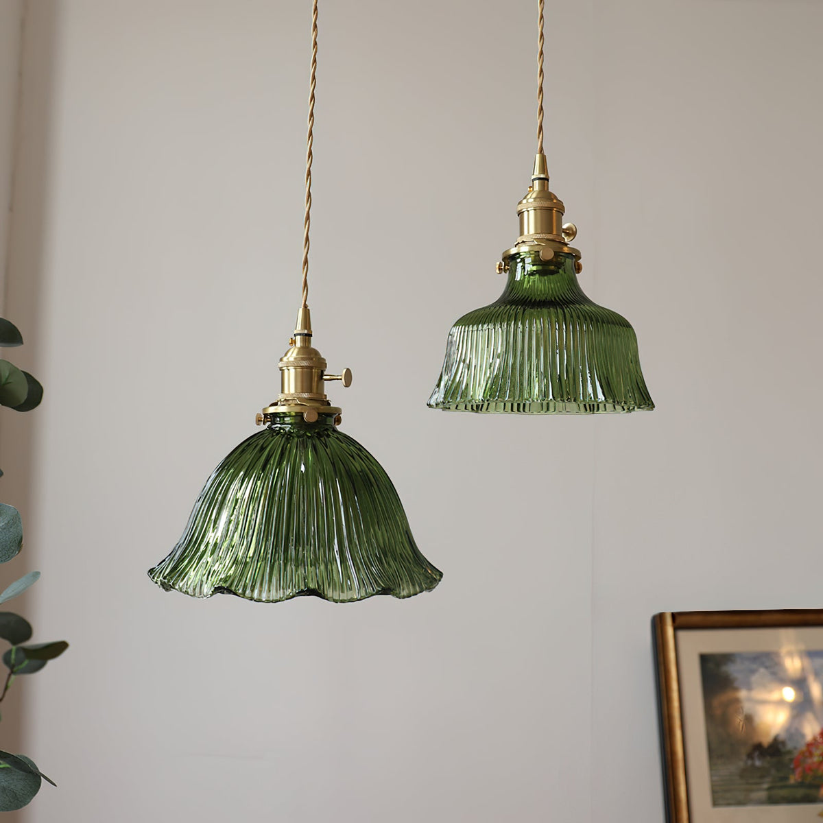 Two green fluted glass pendants with brass cord fittings hanging near a leafy plant and a framed picture, from Clérachic.
