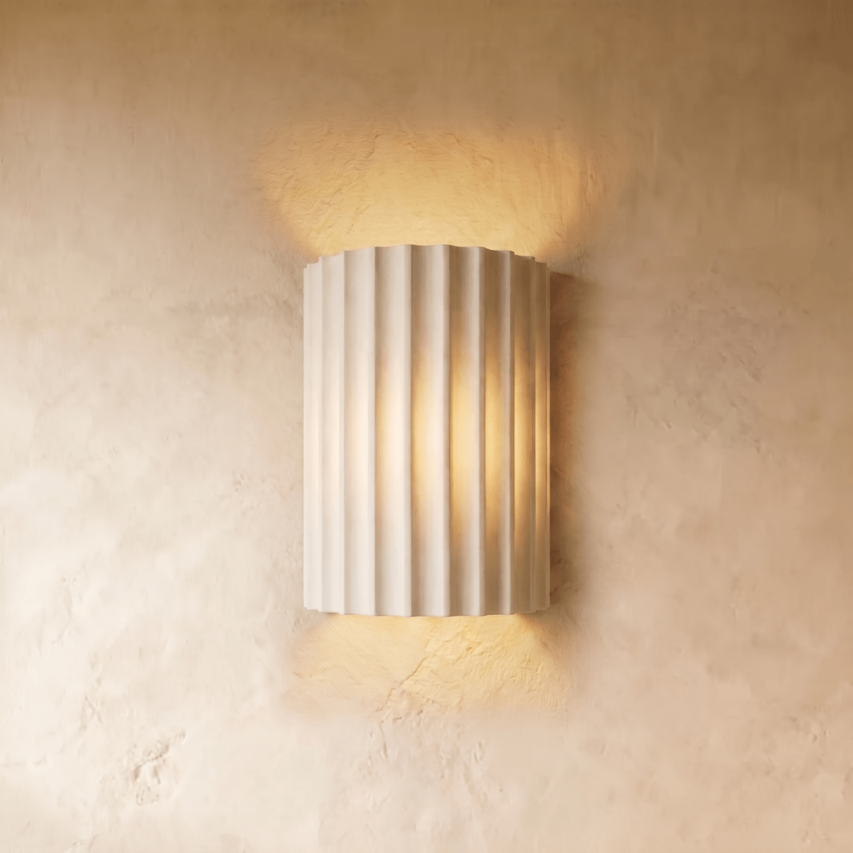 Clérachic wall lamp in white, its fluted half-cylinder shade glowing warm up and down a plaster wall.
