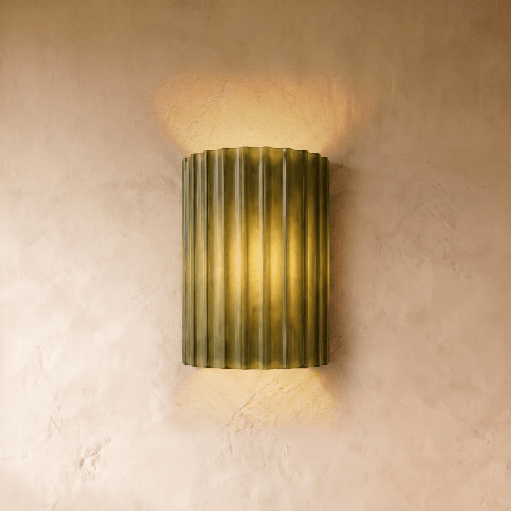 Clérachic wall lamp in olive green, fluted half-cylinder shade lit warm against a plain plaster wall.