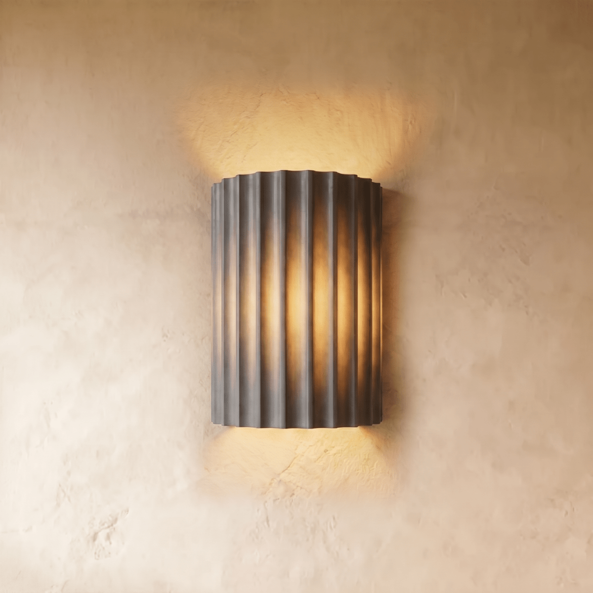 Clérachic wall lamp in gray, its fluted half-cylinder shade glowing warm against a plaster wall.