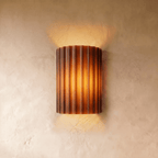 Clérachic wall lamp in burnt orange, fluted half-cylinder shade lit warm against a plaster wall.