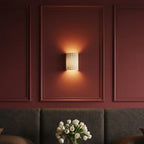 Clérachic wall lamp in white glowing warm within a burgundy wall panel above a tufted headboard and tulips.