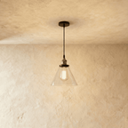 The Clérachic pendant's clear glass cone shade hangs on a black cord, its filament bulb showing through fully.