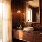 A Clérachic pendant with a clear glass dome shade lights a bathroom vanity with dark tiled walls.