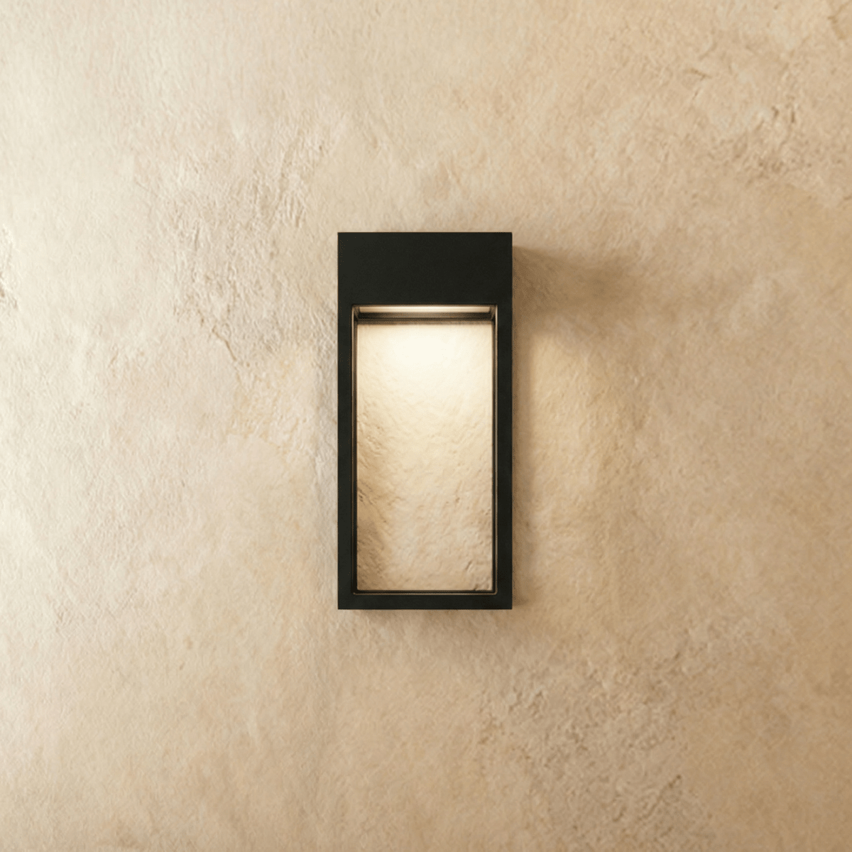 Clérachic grey steel wall sconce lit from within, warm light filling its open rectangular frame on a plaster wall.