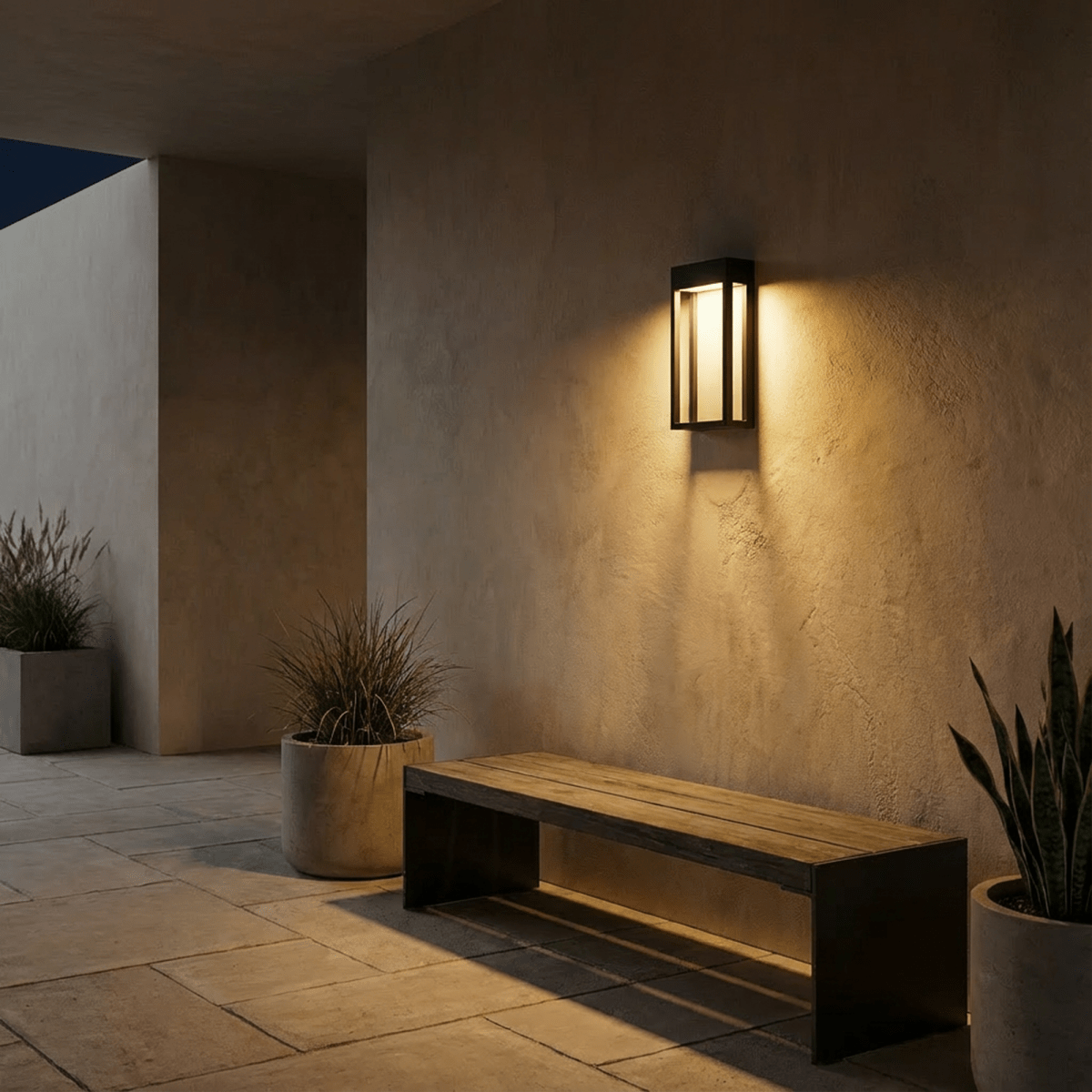 Clérachic grey steel wall sconce glowing warmly above a wooden bench and potted plants on an evening patio.