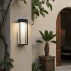Close view of the lit Clérachic grey steel wall sconce beside climbing vines near an open timber door at dusk.