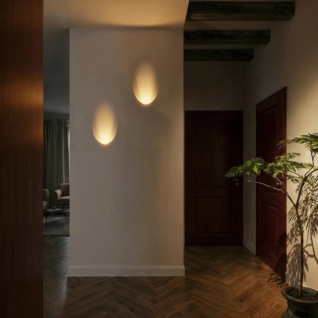 Two Clérachic trimless wall sconces cast warm oval pools of light along a dark hallway wall at night.