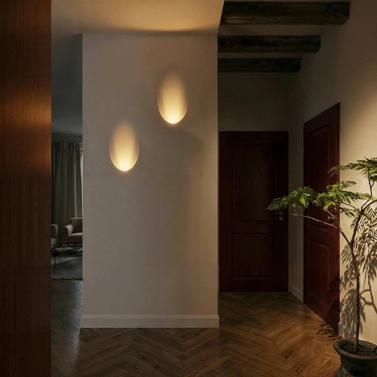 Two Clérachic trimless wall sconces cast warm oval pools of light along a dark hallway wall at night.
