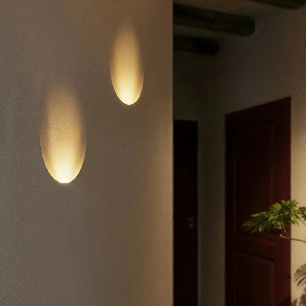 A closer hallway view shows the Clérachic sconce's warm oval glow above patterned tile flooring near a plant.