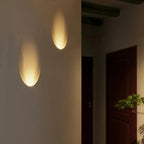 A closer hallway view shows the Clérachic sconce's warm oval glow above patterned tile flooring near a plant.