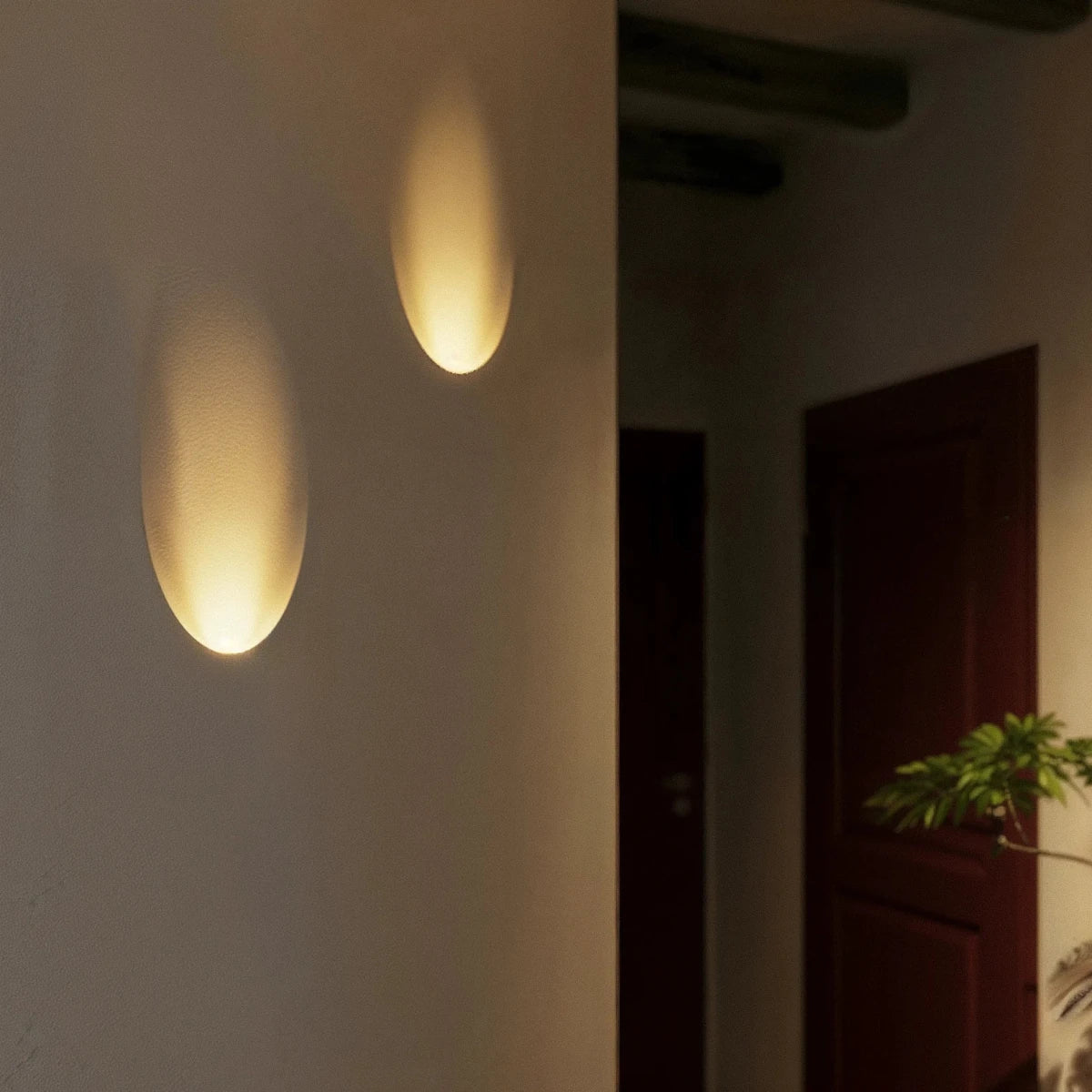 A closer hallway view shows the Clérachic sconce's warm oval glow above patterned tile flooring near a plant.