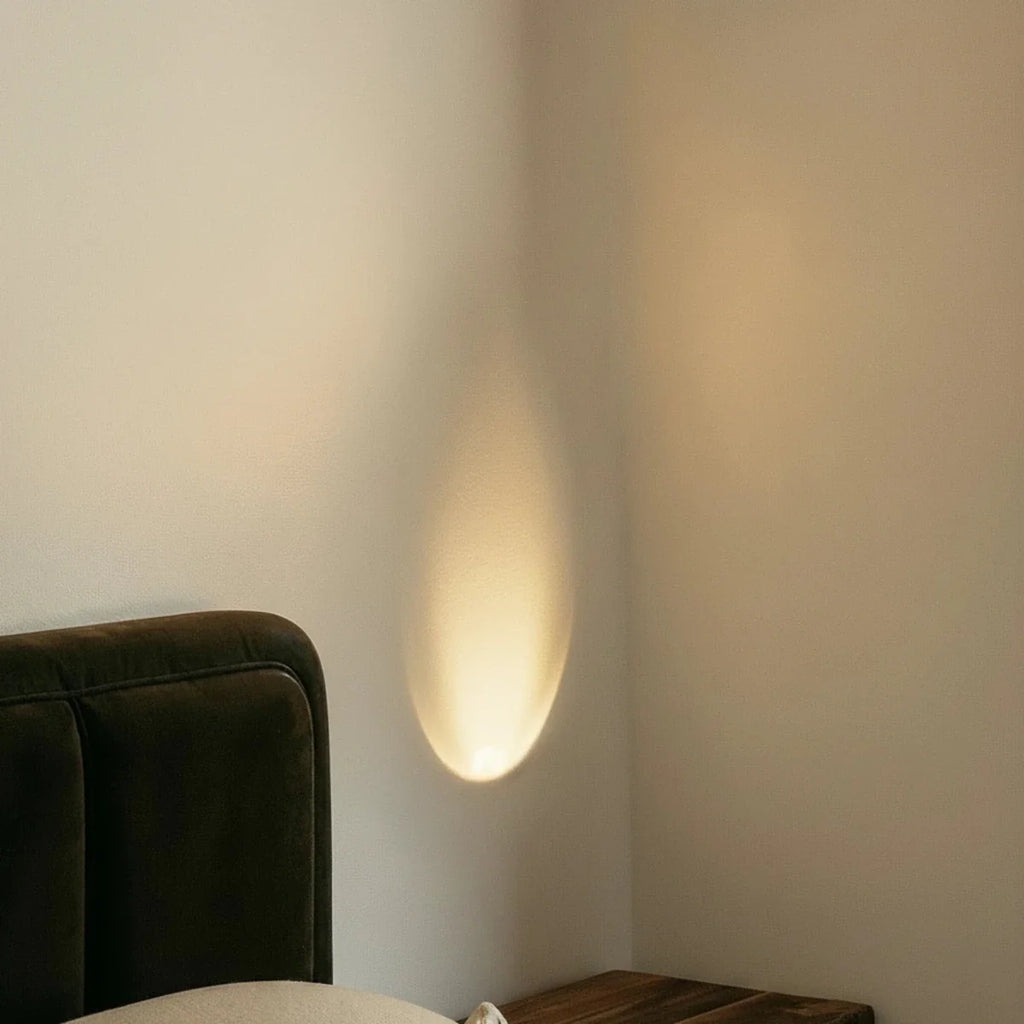 A close view shows the Clérachic sconce's teardrop glow lighting the wall above a bedside nightstand.