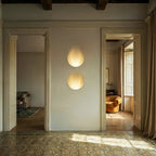 Two stacked Clérachic trimless wall sconces glow warmly in a hallway between two open doorways at sunset.