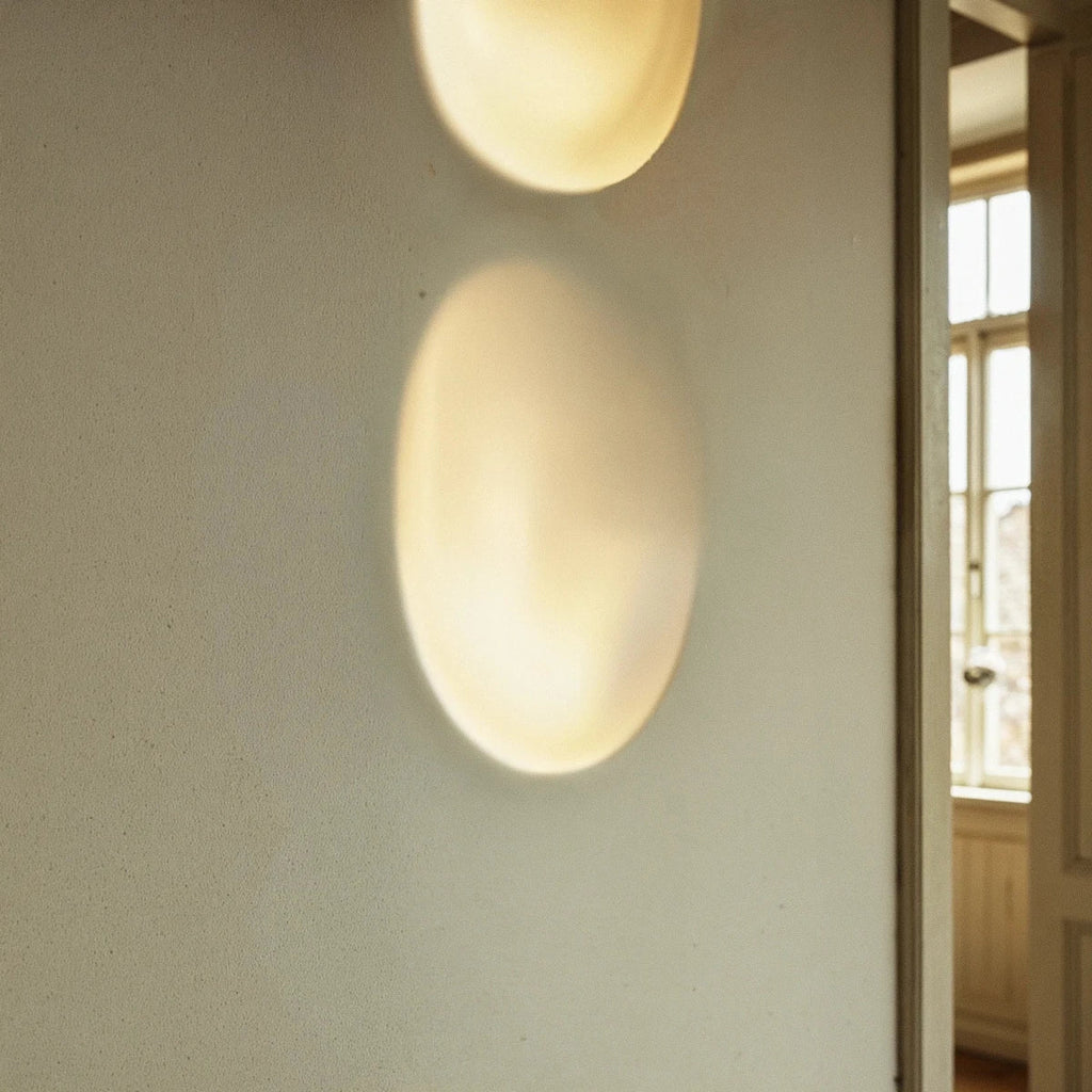 This tight crop highlights the Clérachic sconce's warm glow stacked low on a plaster wall beside a window.