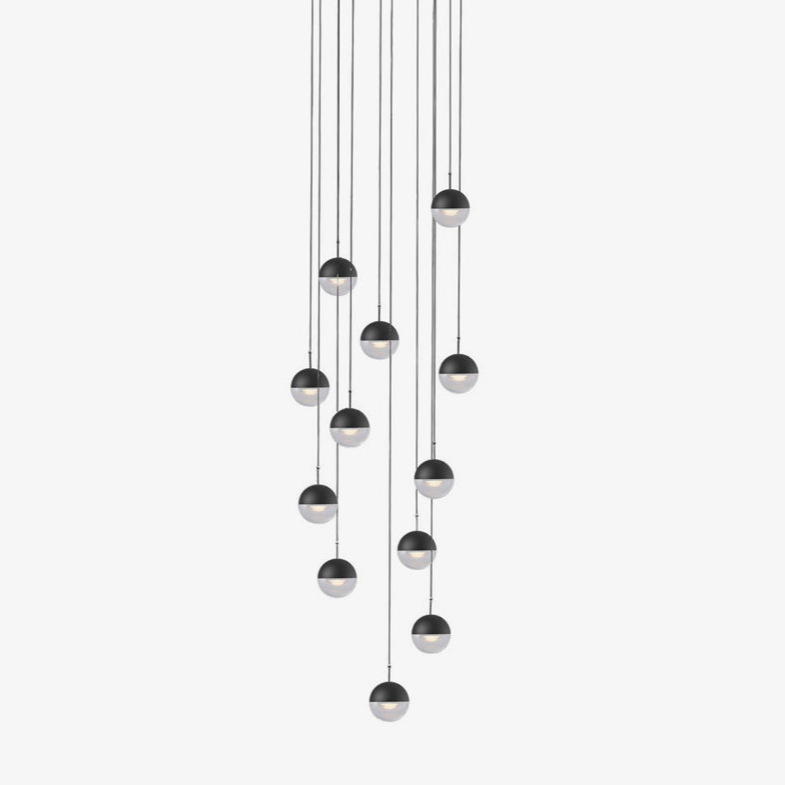 Cluster of twelve Clérachic pendants with matt black caps and clear glass lower halves, hung at varied heights on a white backdrop.