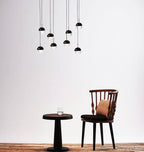 Cluster of Clérachic pendants with matt black caps and clear lower halves above a small black table and a spindle-back chair.