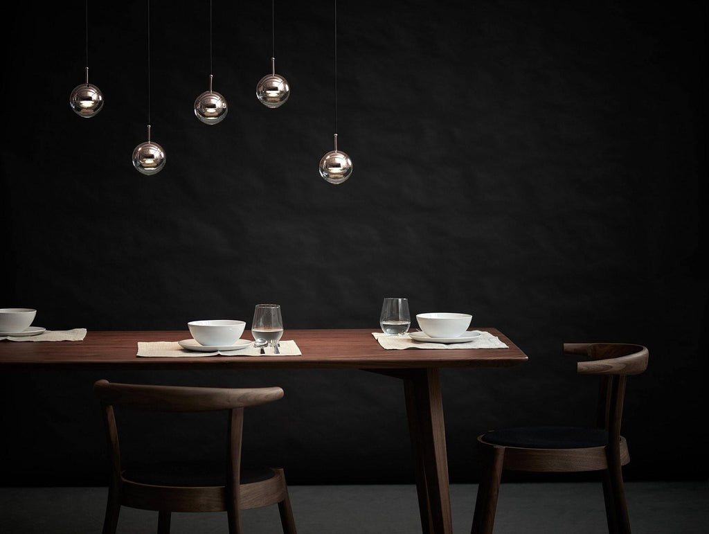 Five small Clérachic globe pendants at different heights against a dark wall, above a dark wooden dining table set for two.