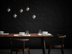 Five small Clérachic globe pendants at different heights against a dark wall, above a dark wooden dining table set for two.