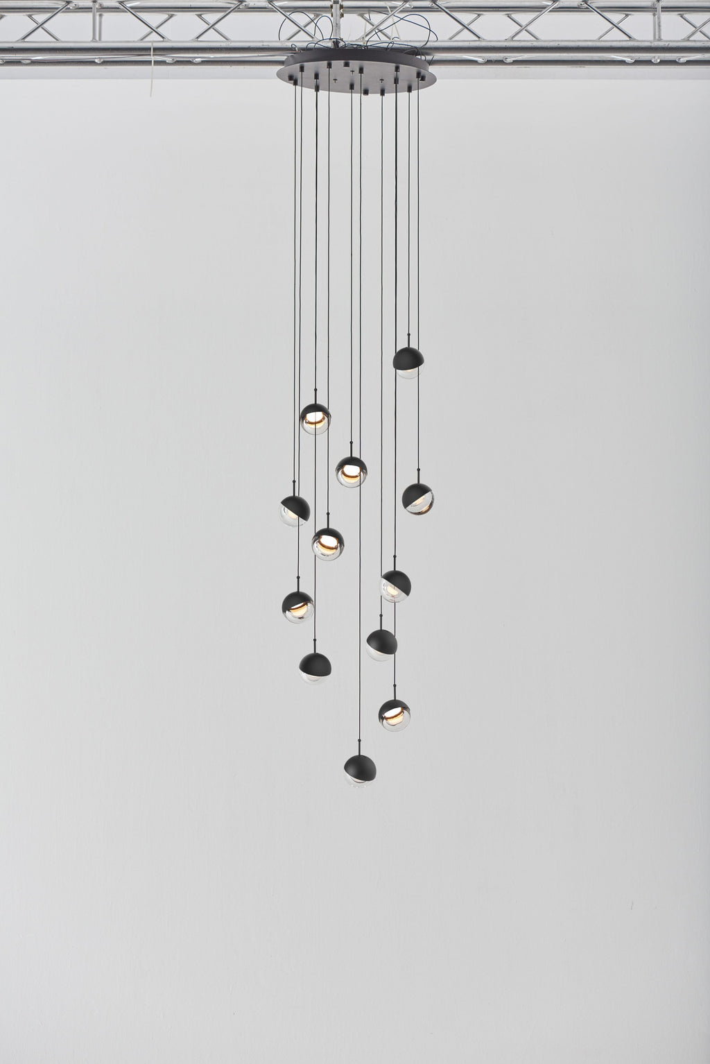 Clérachic pendant cluster with matt black caps hung from a round black ceiling plate against a pale grey wall.