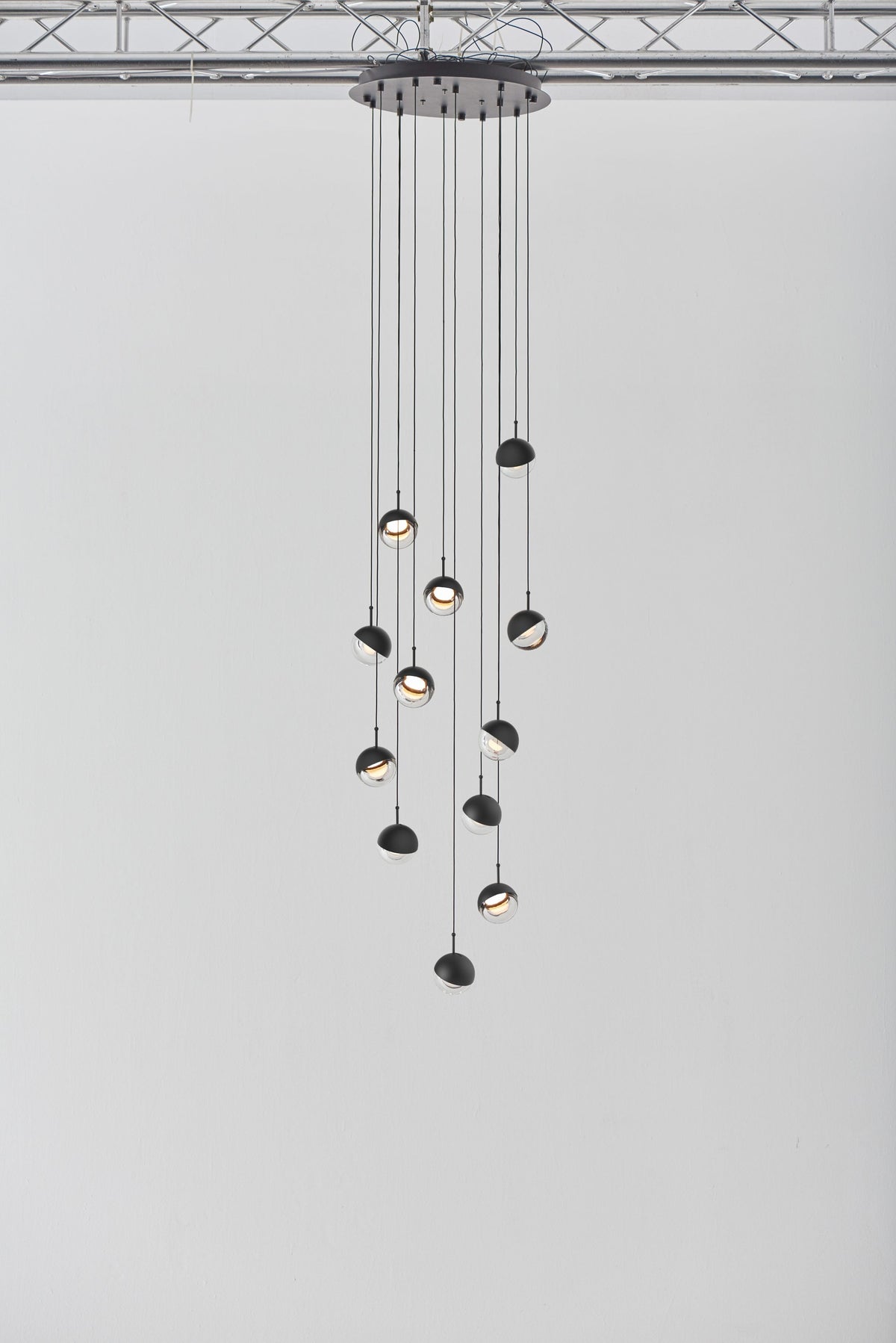 Clérachic pendant cluster with matt black caps hung from a round black ceiling plate against a pale grey wall.
