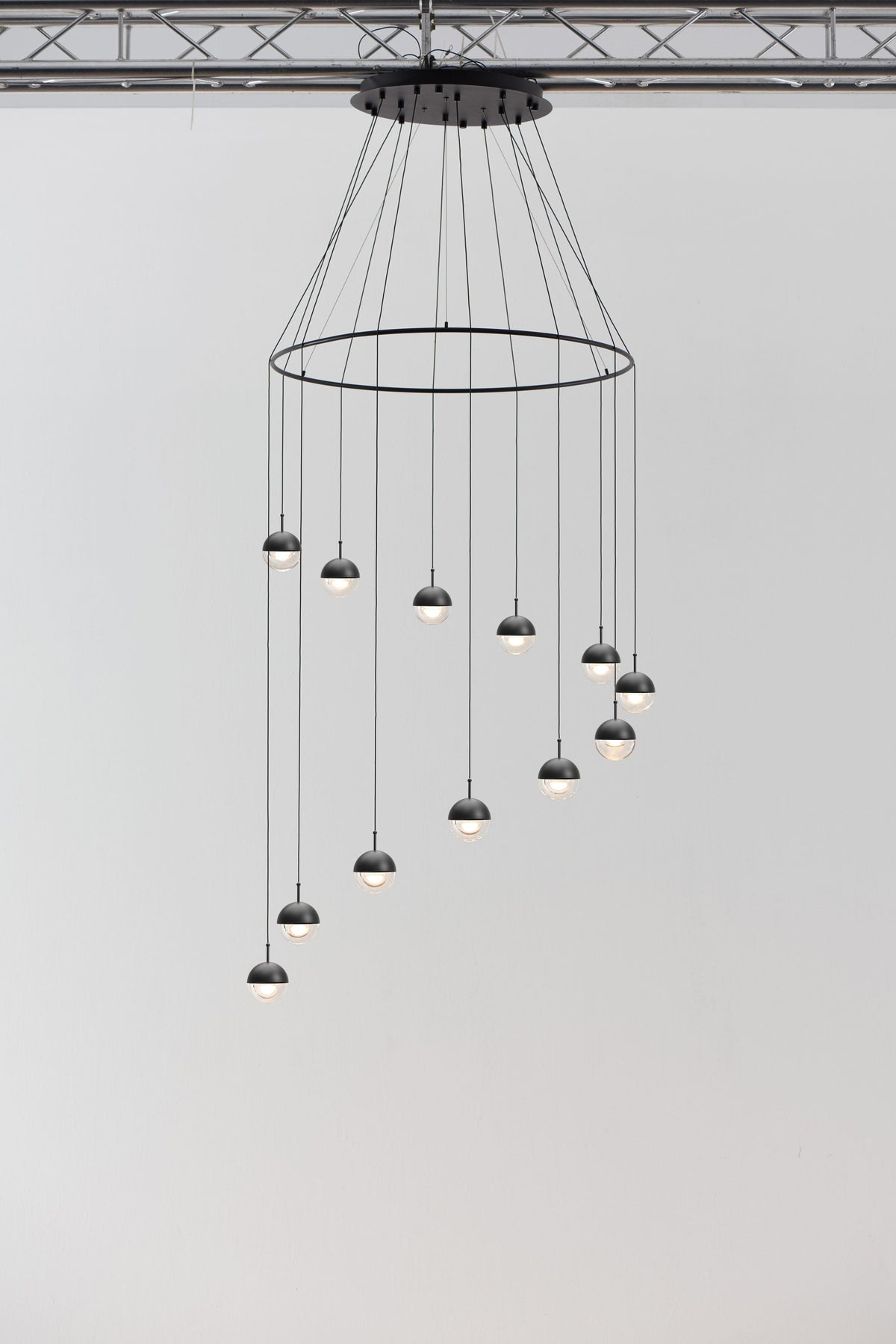 Clérachic ring chandelier with small matt black globe pendants at varied heights, hung under a metal truss.
