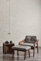 Single gold-finish Clérachic globe pendant against a white brick wall, above a leather armchair and a footstool.