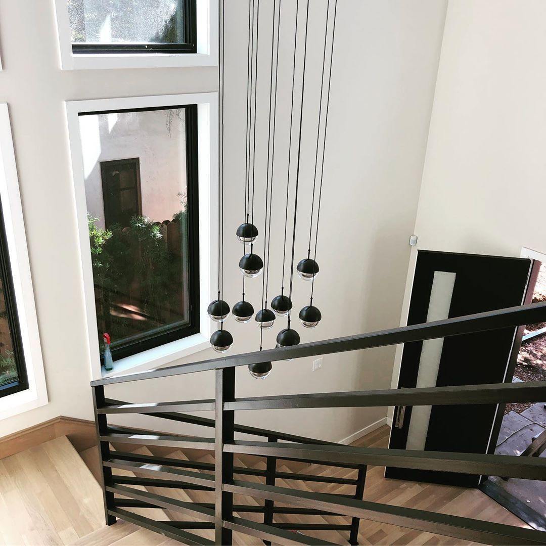 Clérachic pendants with black caps on long cords in a tall stairwell, seen from above past a dark metal railing.