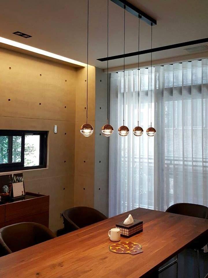 Row of rose gold Clérachic globe pendants on a black rail above a wooden table, beside tall windows with sheer curtains.