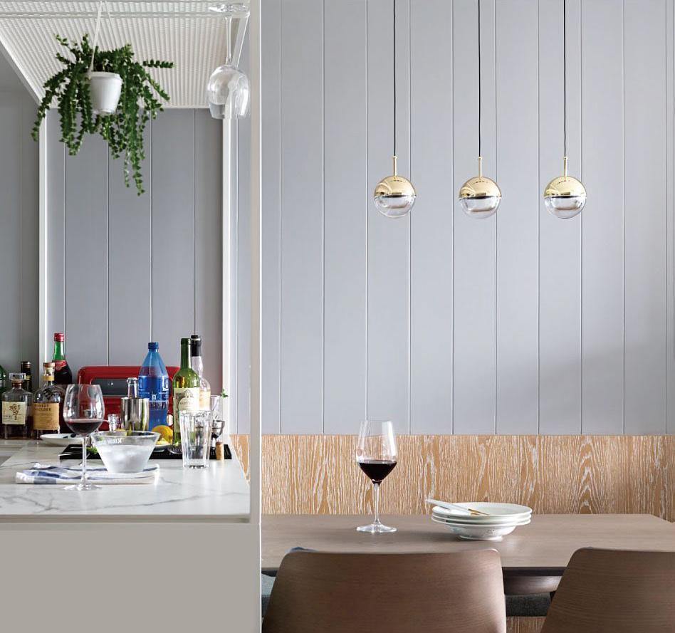 Three gold-finish Clérachic globe pendants in a row against a pale panelled wall, above a table with a wine glass.