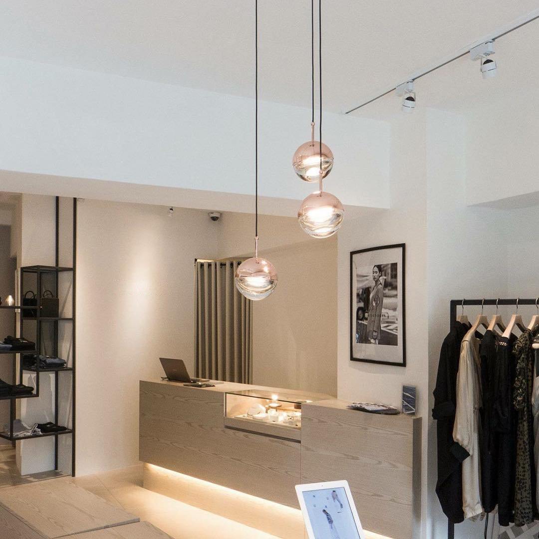 Rose gold Clérachic globe pendants lit above a shop counter, with a clothes rail and a framed photograph beyond.