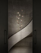 Small Clérachic globe pendants hung at stepped heights down a curved concrete stairwell, with a dark door either side.