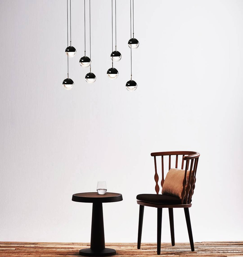 Cluster of Clérachic pendants with matt black caps hung above a small round table and a spindle-back chair.