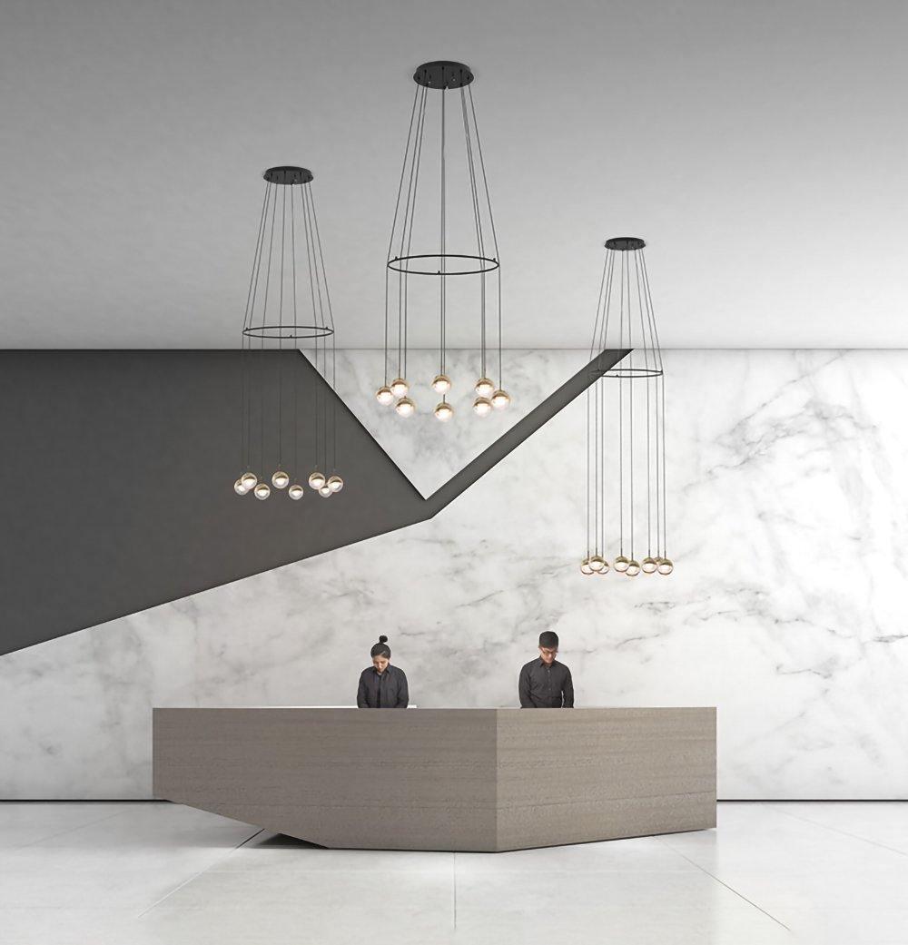 Three Clérachic ring-and-cord chandeliers of gold-toned globes above a reception desk in front of a marble wall.