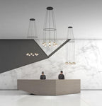 Three Clérachic ring-and-cord chandeliers of gold-toned globes above a reception desk in front of a marble wall.