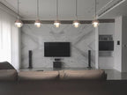 A row of Clérachic globe pendants across a living room, in front of a marble wall with a wall-mounted television.