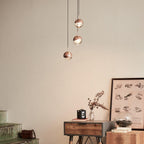 Three rose gold Clérachic globe pendants above a wooden console, a framed print and a vintage camera.