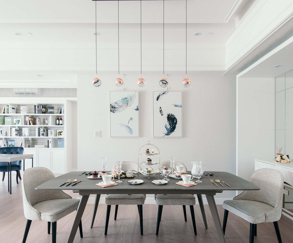 Five Clérachic globe pendants hung in a row over a set dining table, with feather prints and white shelving behind.