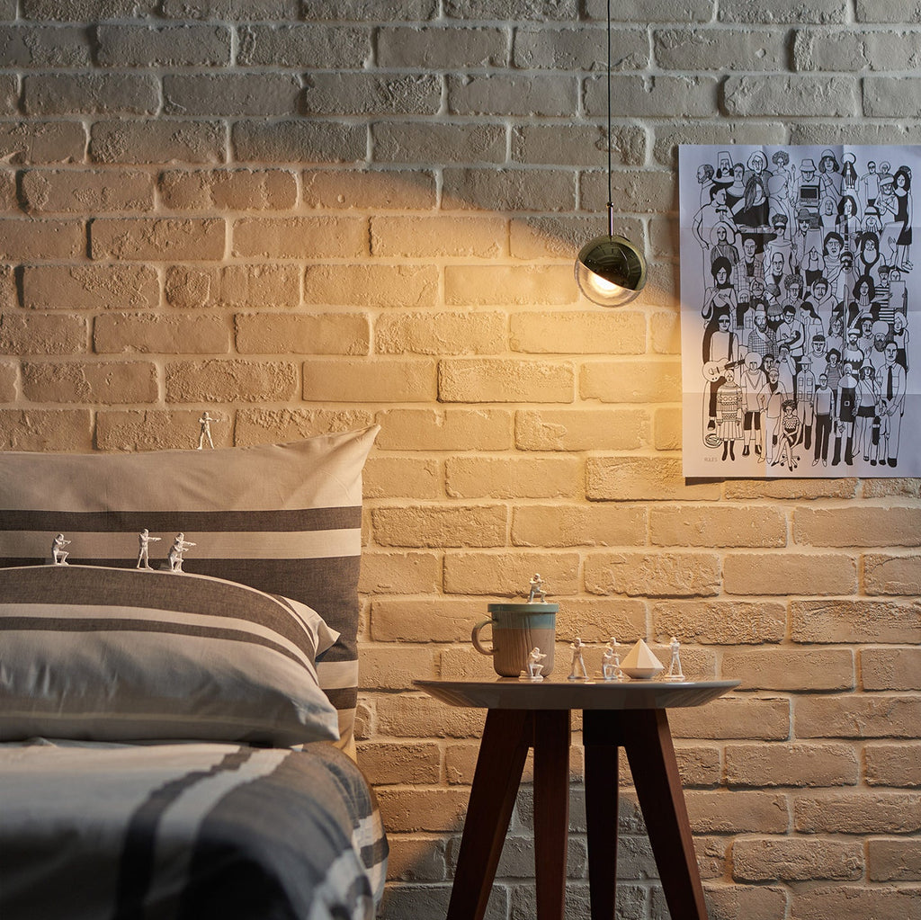 Clérachic globe pendant lighting an exposed brick wall, above a round side table with a mug and small figurines.