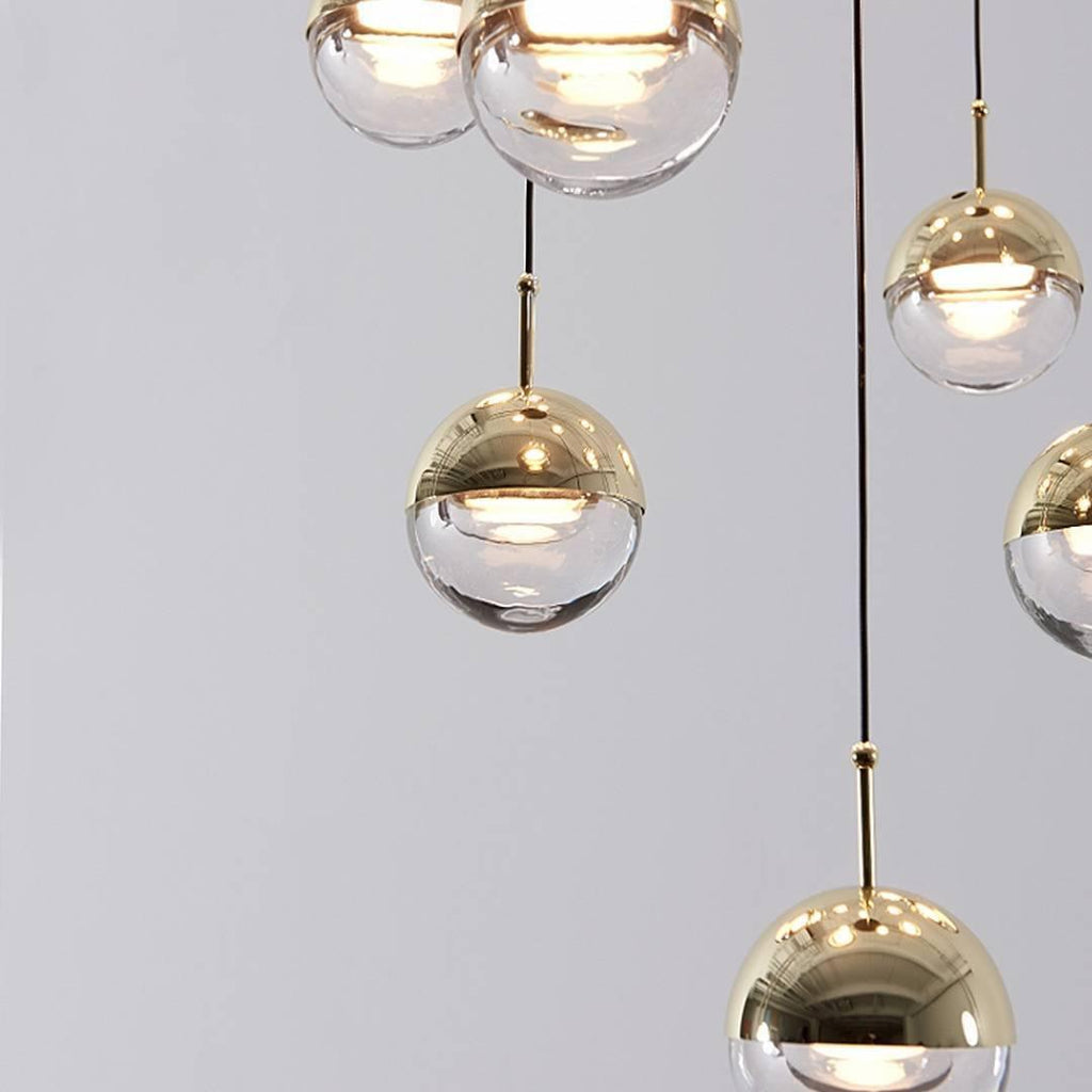 Close view of gold-finish Clérachic globe pendants, with a brass-toned cap, a clear glass half and a lit LED inside.